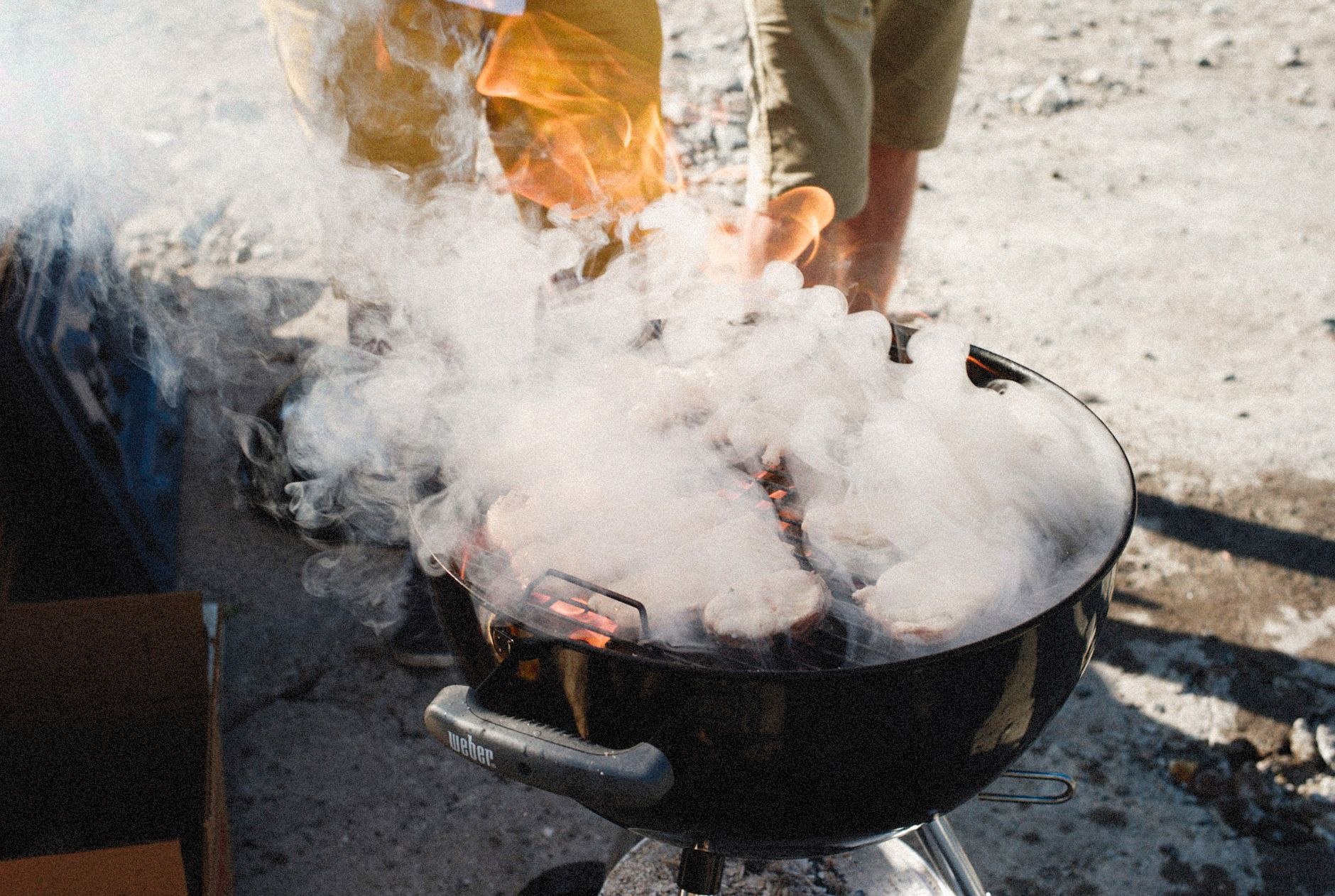 Grilling meat on a smoky barbecue grill outdoors on a sunny day.